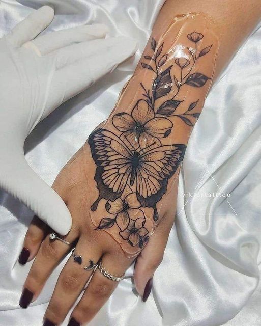 Tatuaje de Hermosa Mariposa Negra en mano con Flores Hojas